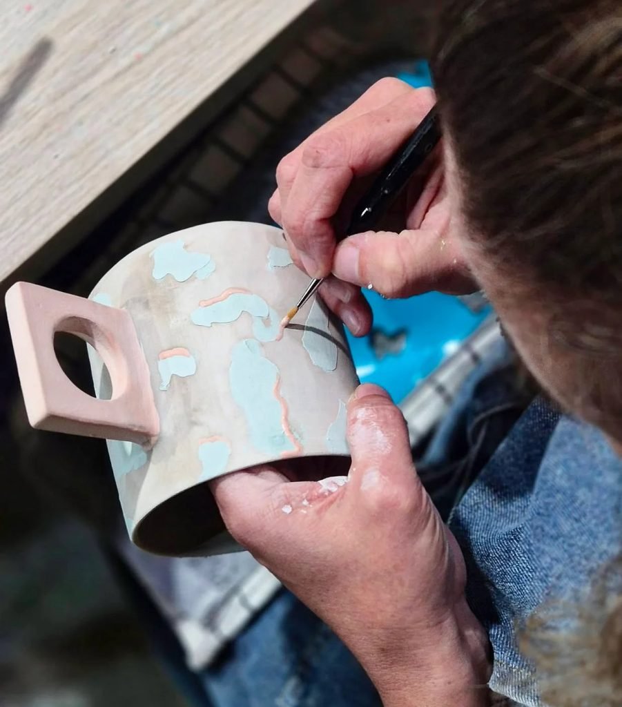 Woman painting personalized ceramic mug with underglazes during creative workshop in Lisbon