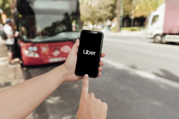 Person holding a smartphone displaying the Uber app logo on a city street