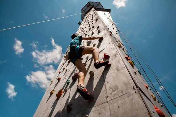 Climber ascending wall beneath Ponte 25 de Abril bridge unique climbing experience Lisbon